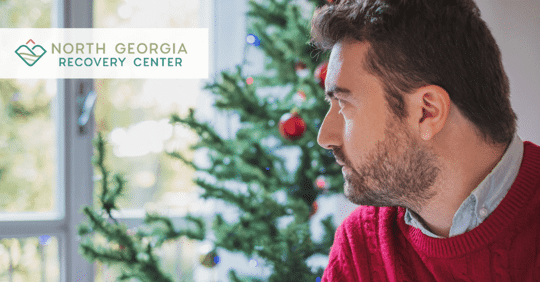 Man looking out the window, wearing a red sweater in front of a Christmas tree